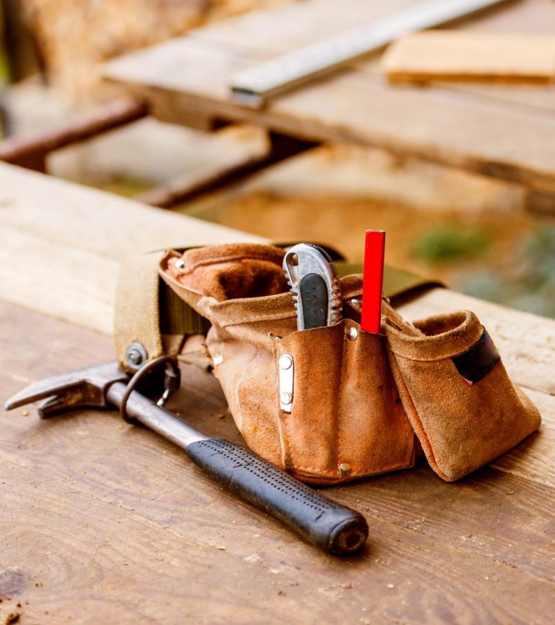 Carpenters bag with belt full of tools laid on wooden table. Construction site.